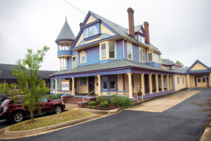 antebellum mansion with a wrap around front porch painted purple and yellow