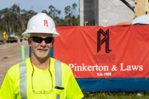 construction worker wearing a yellow vest and white hat standing in front of the pinkerton and laws banner on a fence around a hotel under construction